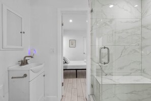 Un baño moderno con lavamanos, espejo y ducha blancos.