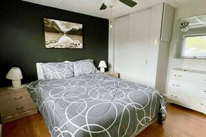 Une chambre Ă coucher comprenant un lit, une table de chevet, une commode, un ventilateur de plafond et une fenĂȘtre.