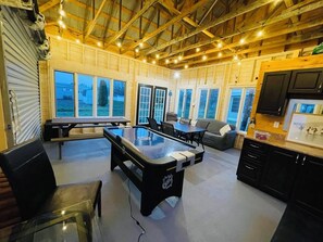 A spacious indoor area with a pool table, seating, and a kitchen area.
