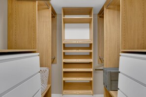 Un vestidor con estanterías y cajones de madera, una cesta de ropa blanca y un caja de almacenamiento gris.