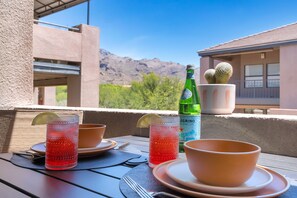 Ein Tisch ist gedeckt mit einem Glas rotem Getränk, einer grünen Flasche und einem Topf mit einem Kaktus auf einem Balkon mit Blick auf die Berge.