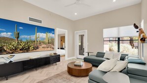 A modern living room with a large cactus mural, a sofa, a coffee table, and a TV. - Luz de Ventana | Redesigned 2BR Condo · Pools + Fitness · Mountain Views (Tucson)