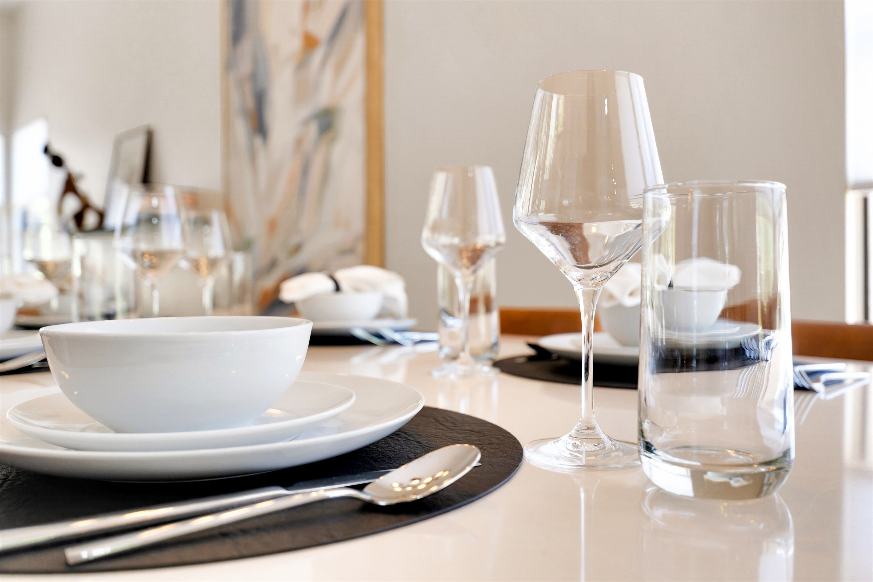 Une table à manger dressée avec de l’assiette blanche, de la verrerie transparente et un saladier blanc.