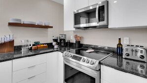 A modern kitchen with white cabinets, a stainless steel stove, a microwave, and a toaster. - Luz de Ventana | Redesigned 2BR Condo · Pools + Fitness · Mountain Views (Tucson)