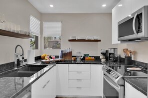A modern kitchen with a central island, stainless steel appliances, and a window with blinds. - Luz de Ventana | Redesigned 2BR Condo · Pools + Fitness · Mountain Views (Tucson)