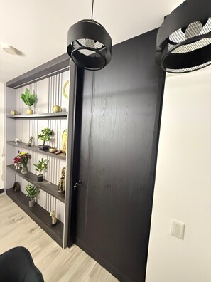 Um quarto com porta de madeira escura, parede branca e prateleira com plantas e objetos decorativos.