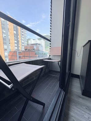Varanda com uma cadeira, uma mesa e vista para prédios.