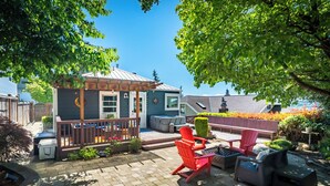 En uteplats med utemöbler, en liten överbyggd struktur och utsikt över ett hus i bakgrunden.