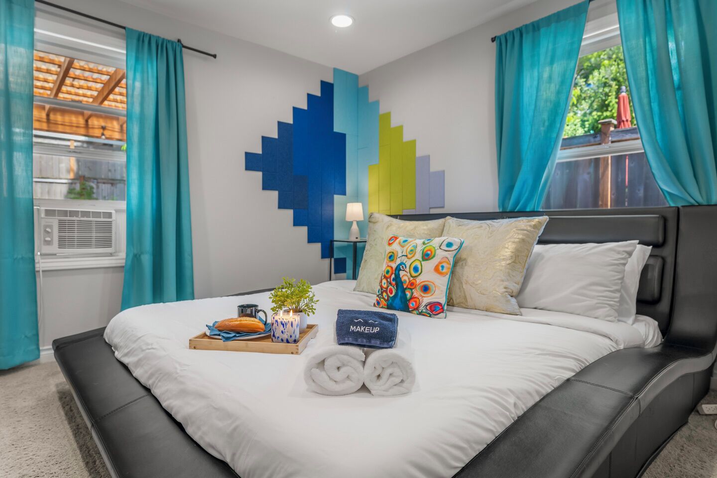 A modern hotel room with a bed, a tray with breakfast items, a towel, and a wall with a geometric pattern.