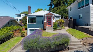 Ett bostadshus med en röd dörr, en liten framträdgård med lavendelplantor och ett hus som står intill.