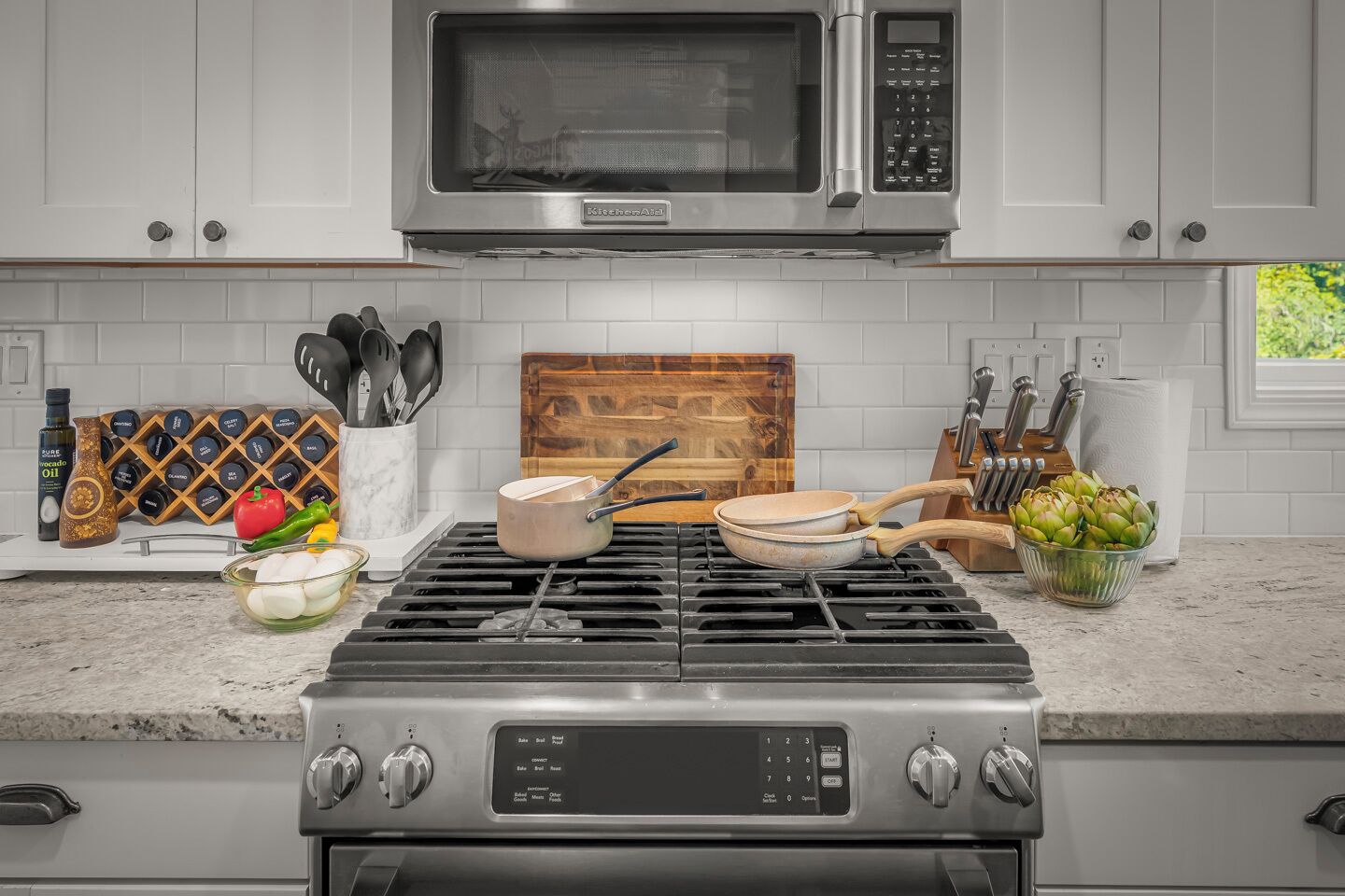 A kitchen with a gas stove, a microwave, a knife block, and a cutting board.