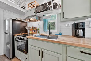 A kitchen with a refrigerator, stove, oven, coffee maker, and a window with curtains.