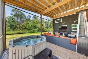 A hot tub with a wooden deck, outdoor seating, and a view of the surrounding greenery.