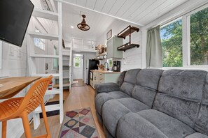 A modern kitchen with white cabinetry, a dining table with orange chairs, and a grey sofa.