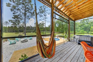 A hammock hanging inside a covered deck with a view of a forest and outdoor seating area.