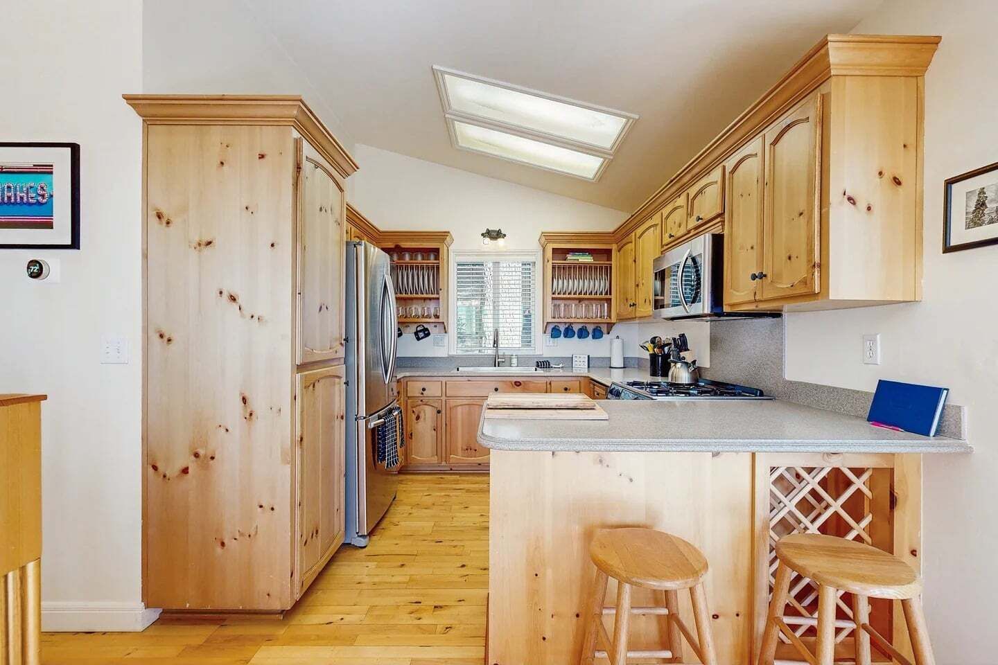 A kitchen with wooden cabinets, a refrigerator, a microwave, and a stove. There is a window with blinds and a ceiling light.