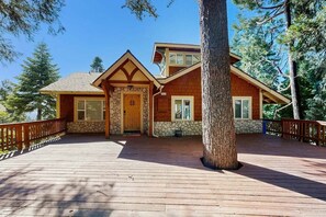 A two-story wooden house with a stone facade, a wooden deck, and a large tree in the foreground. - Pinetree Palace | Mountain Retreat | Games | Treetop Views | Sleeps 6 (Lake Arrowhead)