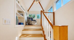 Un escalier avec des marches en bois et une rampe en bois, menant à une pièce où se trouvent une chaise et une bibliothèque.