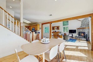 Un grand espace de vie comprenant une table à manger, des chaises, une cheminée et, au fond, une cuisine.