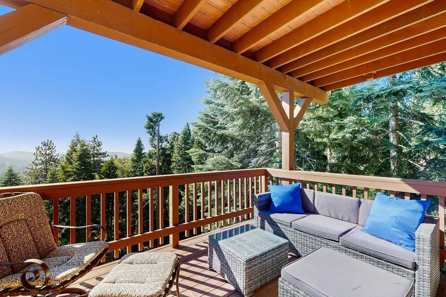 Un espace extérieur aménagé, abrité et doté d'une terrasse en bois, de meubles en osier et offrant une vue sur un paysage boisé.