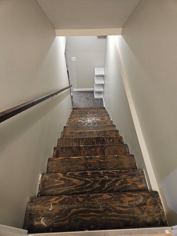 A wooden staircase with a handrail, leading to a landing with a white shelf unit.