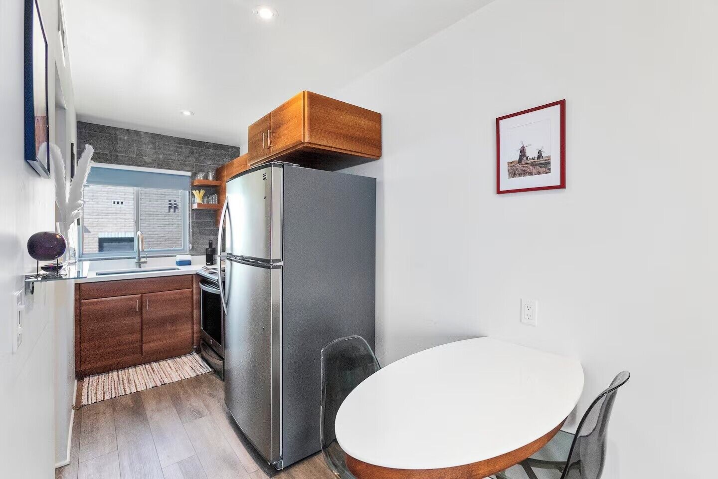 A compact kitchen with a refrigerator, wooden cabinets, a small dining table, and a window.