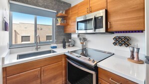 Een moderne keuken met een roestvrijstalen magnetron, oven en spoelbak. Er is een raam met uitzicht op een bakstenen gebouw.