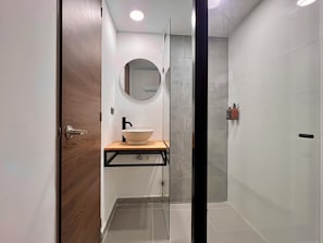 A modern bathroom with a wooden vanity, a round mirror, and a glass shower enclosure. - Makondo House in Provenza by Nowa (Medellín)