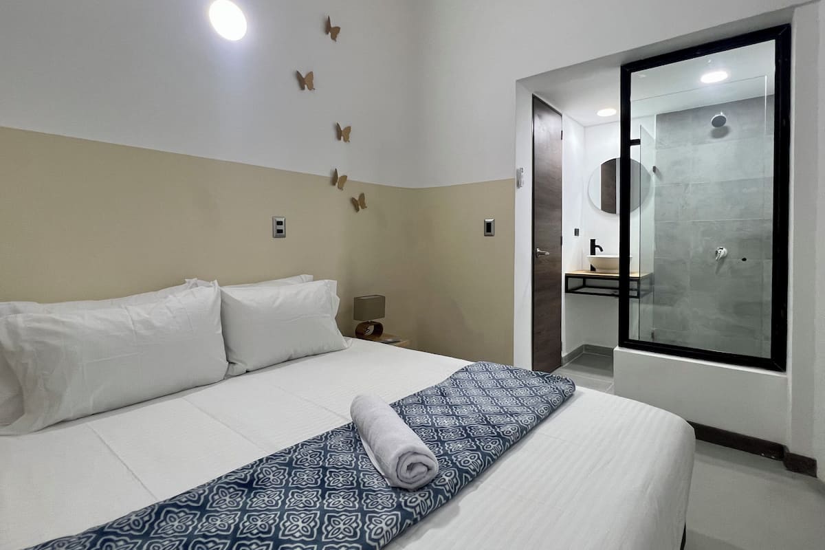Una habitación de hotel con una cama, una mesita de noche, un espejo y un baño visible a través de una puerta abierta.