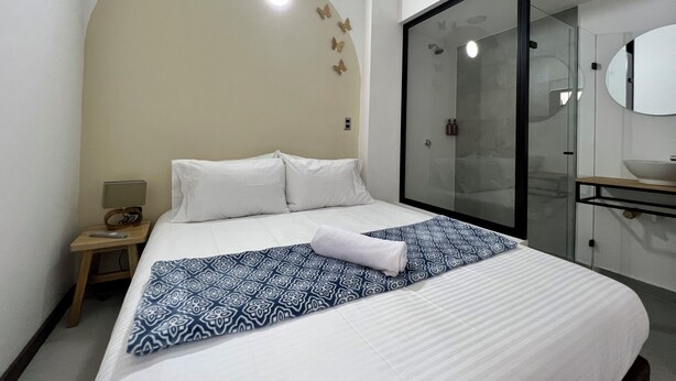 Habitación de hotel con cama, mesita de noche, baño con cabina de ducha de vidrio y espejo.