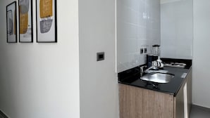 Una cocina moderna con encimera negra, pileta de acero inoxidable y cafetera. Hay tres obras de arte enmarcadas en la pared.