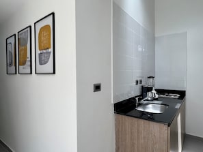 A modern kitchen with a black countertop, stainless steel sink, and a coffee maker. There are three framed artworks on the wall. - Makondo House in Provenza by Nowa (Medellín)