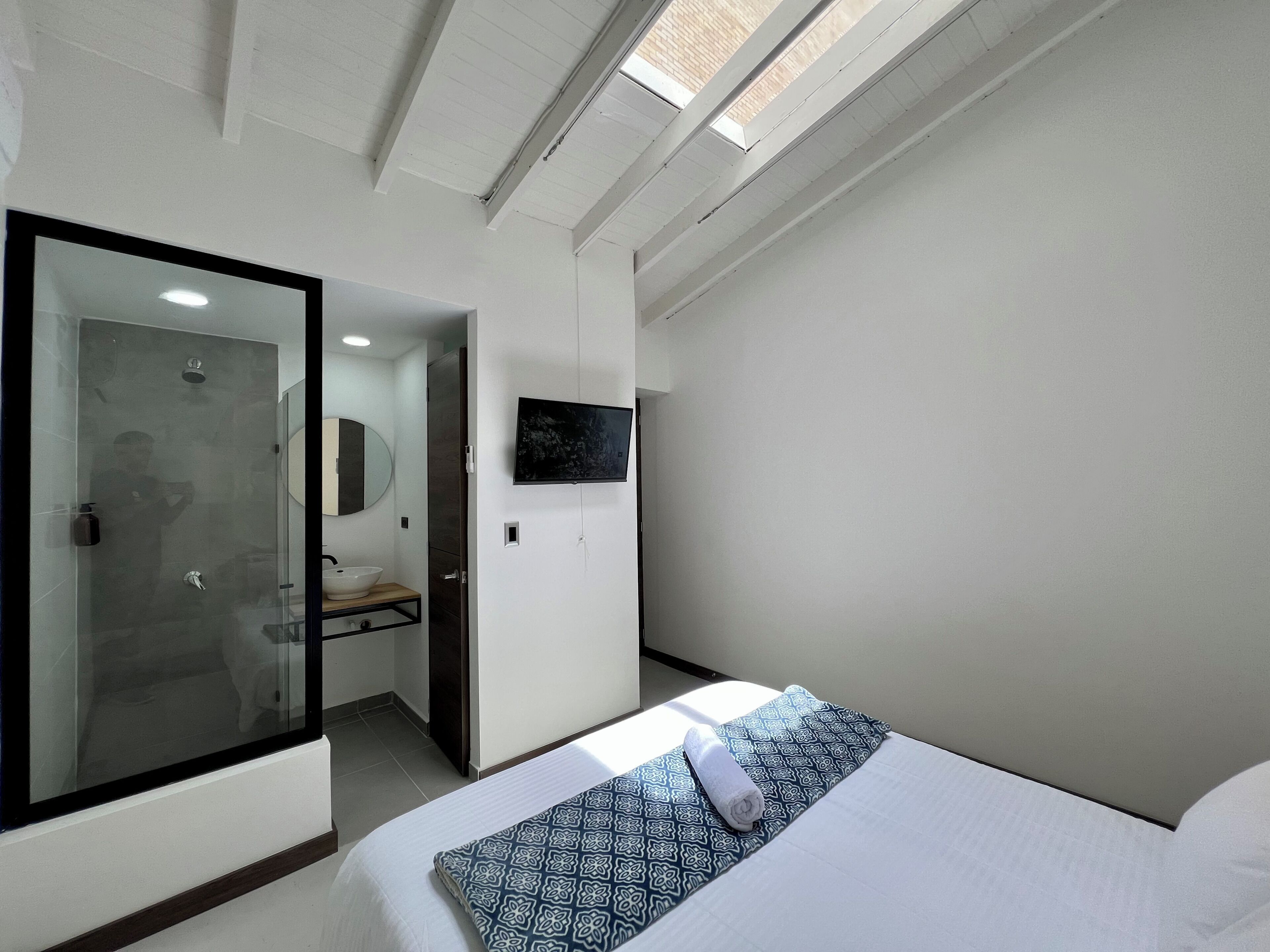 Een moderne hotelkamer met een glazen douchecabine, een wandgemonteerde televisie en een bed met een gestreept kussen.