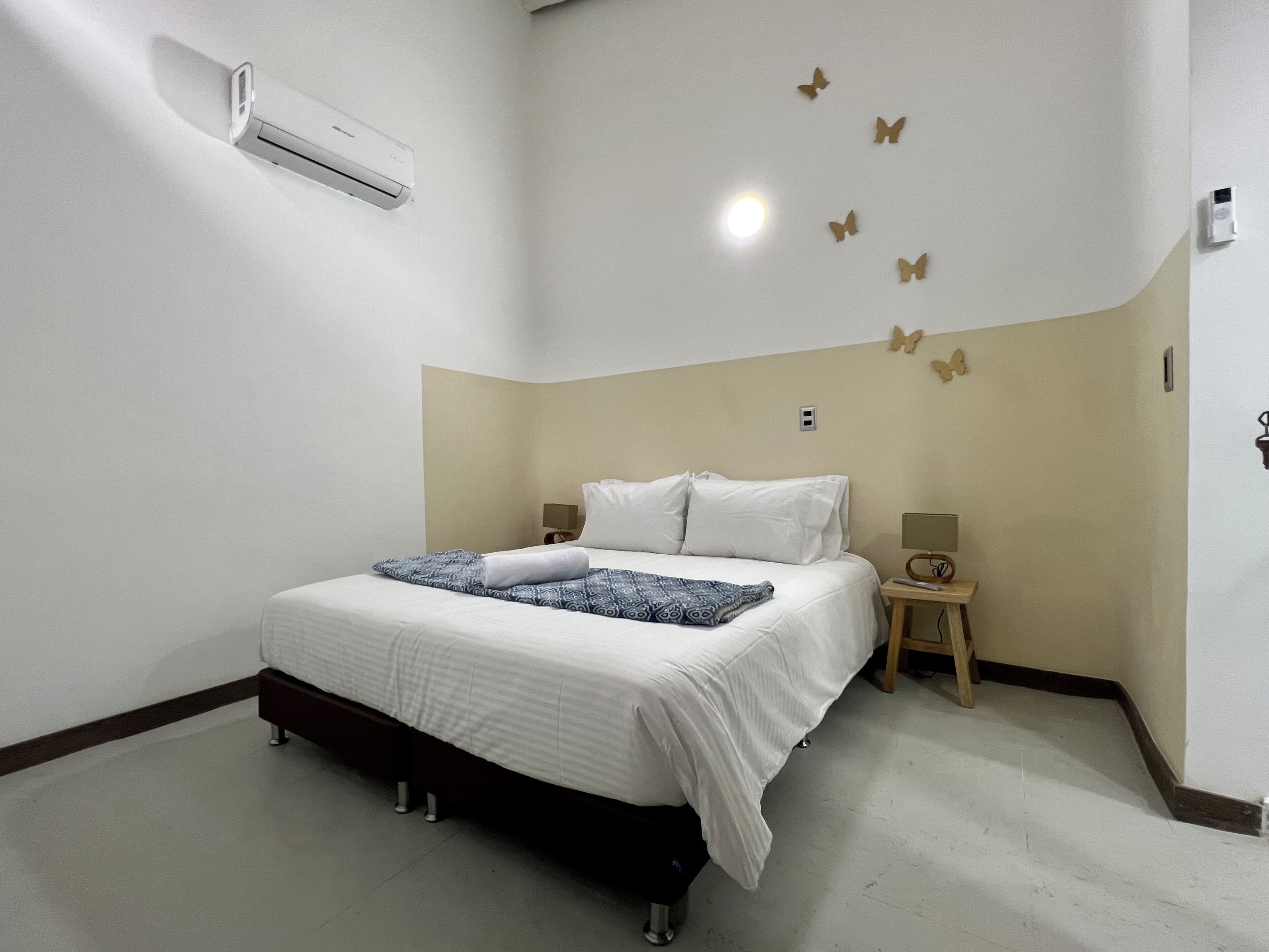 A hotel room with a bed, bedside tables, an air conditioning unit, and wall-mounted butterfly decorations.