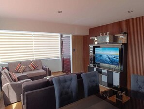 A modern living room with a flat-screen TV, a sofa, and a dining area. - Amazing 5-bedroom apartment in Cusco perfect for your getaway (Cusco)