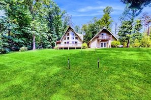 A two-story house with a balcony, surrounded by a well-maintained lawn and trees. - Lake Anna A-Frame | Beach, Dock & Hot Tub | 5BR (Bumpass)