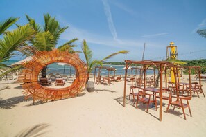 Ein Strand mit einer runden Holzkonstruktion, Liegestühlen und Sonnenschirmen.