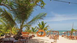 A beach setting with wooden furniture, palm trees, and a circular wooden structure. - Casa De La Puerta Azul (San Felipe Puerto Plata)
