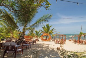 A beach setting with wooden furniture, palm trees, and a circular wooden structure. - Casa De La Puerta Azul (San Felipe Puerto Plata)