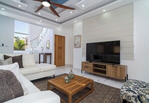 A modern living room with a sofa, coffee table, TV, and a staircase. - Casa De La Puerta Azul (San Felipe Puerto Plata)