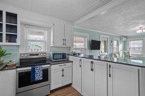 A kitchen with white cabinets, a microwave, an oven, and a window with blinds. - The Lookout at Sandy Sea Star: 2 Bdrm Upper Unit Near Beach Access (Carolina Beach)