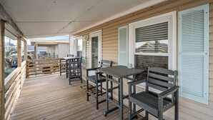 Eine überdachte Terrasse mit Holzgeländer, einem Tisch mit Stühlen und Blick auf ein Haus im Hintergrund.