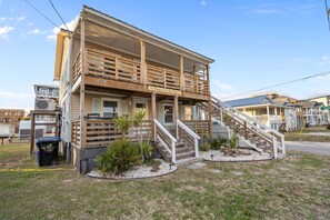 A two-story building with a balcony, a staircase, and a sign reading 'A Wheel On The Beach.' - The Lookout at Sandy Sea Star: 2 Bdrm Upper Unit Near Beach Access (Carolina Beach)
