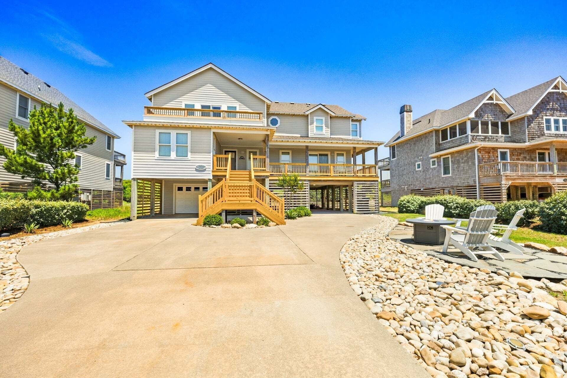 A two-story residential building with a central staircase, a driveway, and a patio area with outdoor seating.