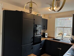 Eine Küche mit einem schwarzen Kühlschrank, einem eingebauten Backofen, einer Kaffeemaschine und einem Fenster mit Blick auf eine Ziegelwand.