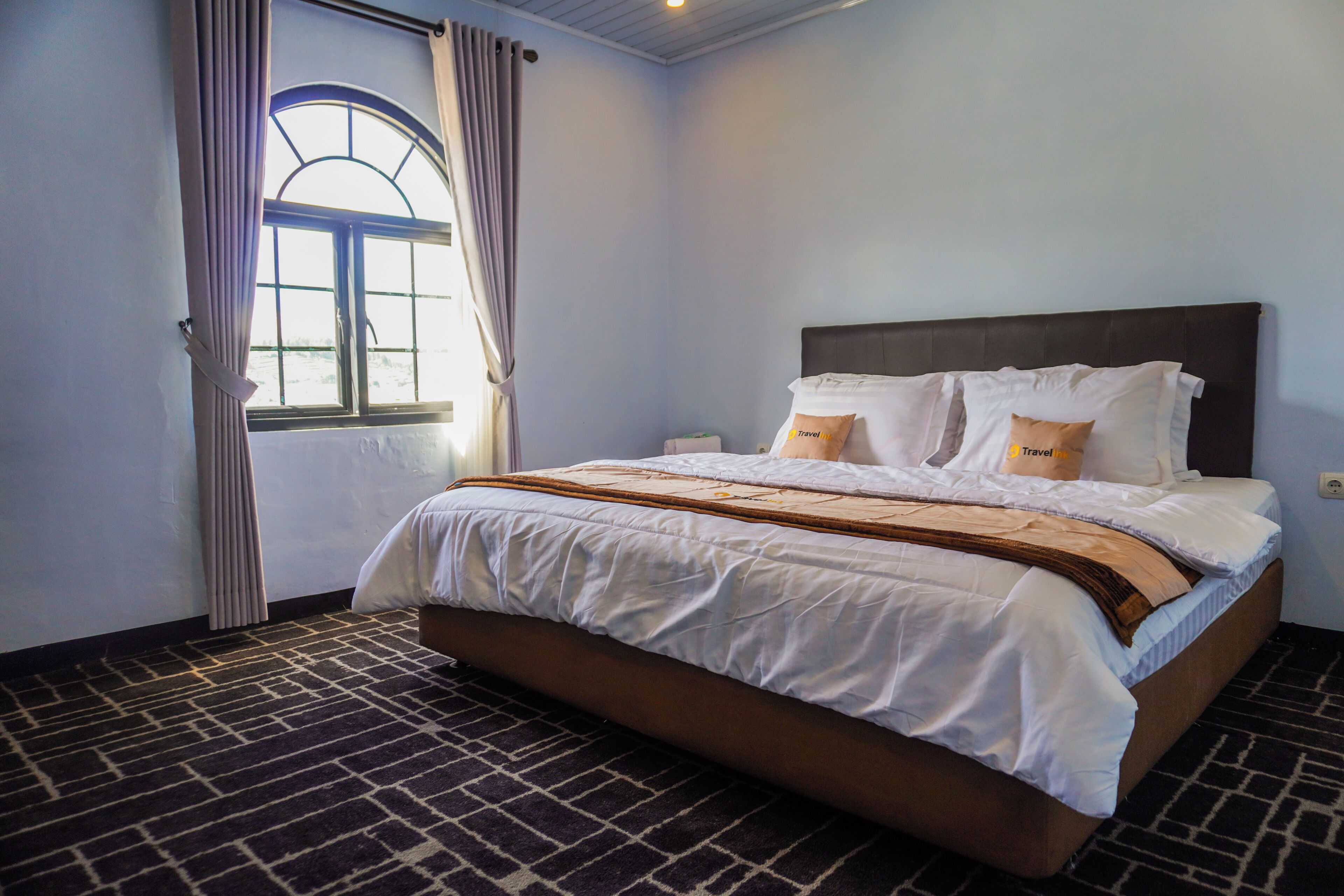 Una camera d'albergo con un letto, tende, una finestra e un tappeto a motivi.