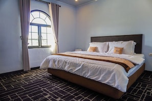 Een hotelkamer met een bed, gordijnen, een raam en een kamerbreed tapijt.