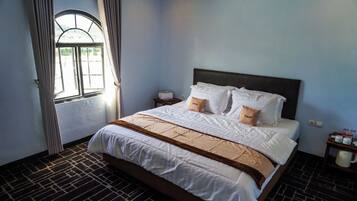 Een hotelkamer met een groot bed, een raam met gordijnen, een nachtkastje met een lamp en een koffiezetapparaat.