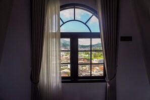 A window with a view of a town, curtains, and a sign on the wall. - Instay Villa Dieng United (Dieng Kulon)