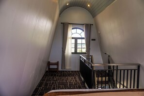 A narrow stairway with a black and white patterned floor, a wooden chair, and a window with curtains. - Instay Villa Dieng United (Dieng Kulon)